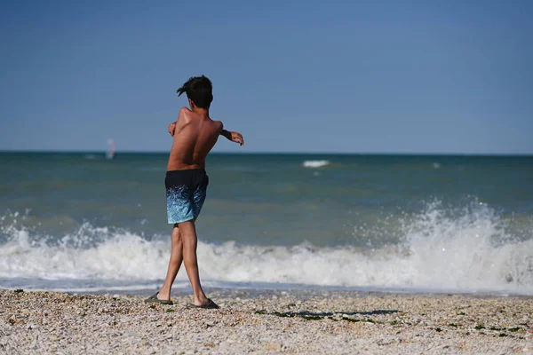 Back of boy throw pebbles into the sea in beach Porto Sant Elpidio, Italy.