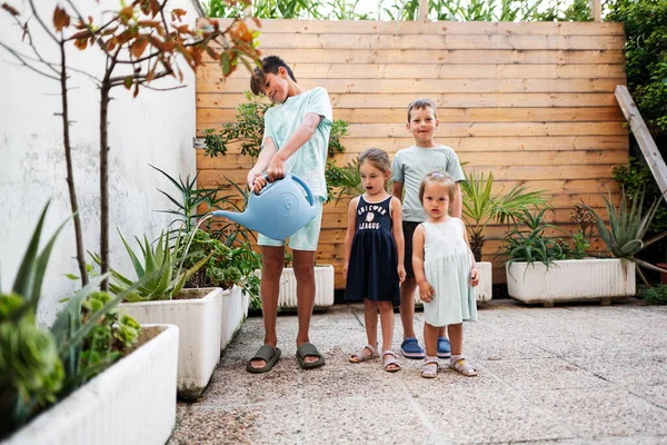 stock image Children with can watering the flowers on the terrace of the house.