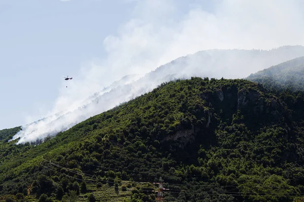 Fire fighting helicopter dropping water on forest fire at mountain in Sant\'Antonio Abate, Campania, Italy.