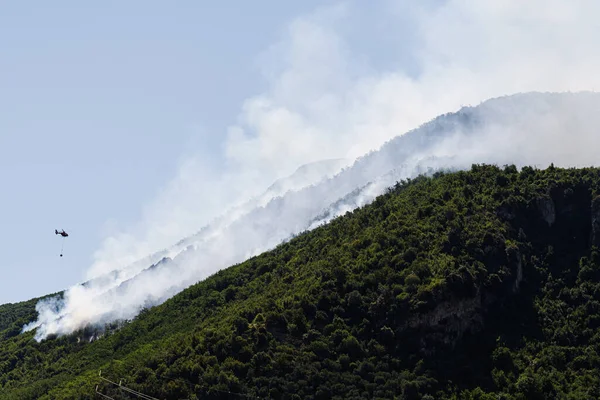 Fire fighting helicopter dropping water on forest fire at mountain in Sant\'Antonio Abate, Campania, Italy.