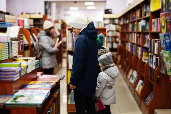 Children in jacket reaching a book from bookshelf at the library. Learning and education of european kids.