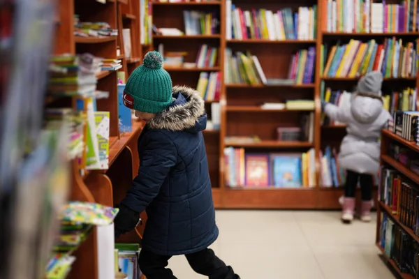 Boy in jacket reaching a book from bookshelf at the library. Learning and education of european kids.