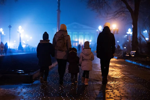 Back of family walking in night foggy city.