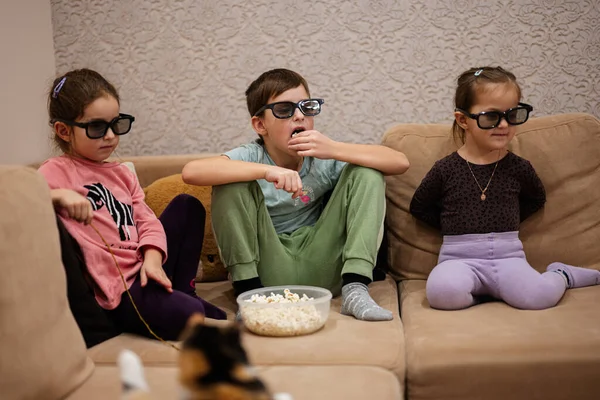 Three children sitting on the living room, wear 3d glasses watching movie or cartoon.