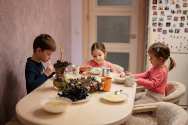 Three kids have dinner together in the kitchen. 