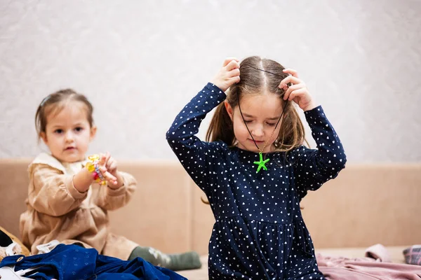 Two sisters are choosing clothes from the wardrobe at home on the sofa. Girl wears a starfish pendant around her neck.