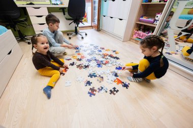 Children connecting jigsaw puzzle pieces in a kids room on floor at home.  Fun family activity leisure. 