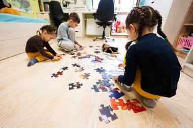 Children connecting jigsaw puzzle pieces in a kids room on floor at home.  Fun family activity leisure. 