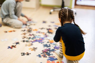 Children connecting jigsaw puzzle pieces in a kids room on floor at home.  Fun family activity leisure. 