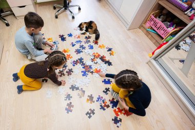 Children connecting jigsaw puzzle pieces in a kids room on floor at home.  Fun family activity leisure. 