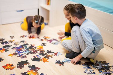 Children connecting jigsaw puzzle pieces in a kids room on floor at home.  Fun family activity leisure. 