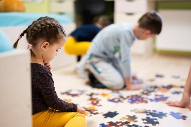Children connecting jigsaw puzzle pieces in a kids room on floor at home.  Fun family activity leisure. 