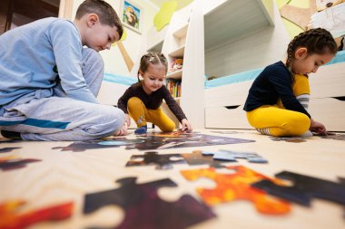 Children connecting jigsaw puzzle pieces in a kids room on floor at home.  Fun family activity leisure. 