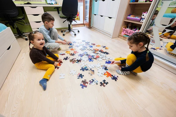 Children connecting jigsaw puzzle pieces in a kids room on floor at home.  Fun family activity leisure. 