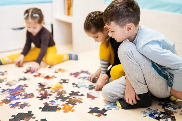 Children connecting jigsaw puzzle pieces in a kids room on floor at home.  Fun family activity leisure. 