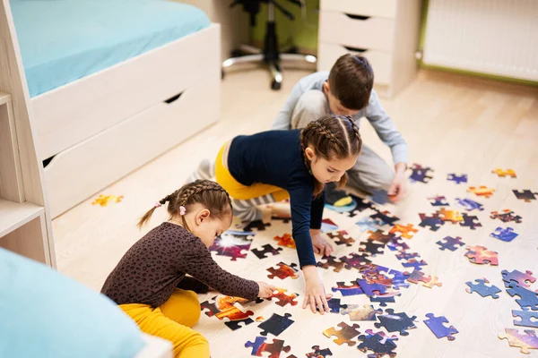 Children connecting jigsaw puzzle pieces in a kids room on floor at home.  Fun family activity leisure. 