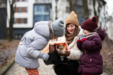 Mother and daughters with cat in travel plastic cage carriage outdoor at park.