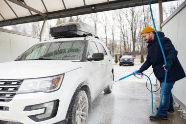 Man washing american SUV car with roof rack at a self service wash in cold weather.