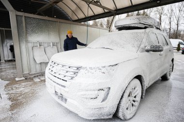 Man washing american SUV car with roof rack at a self service wash in cold weather.