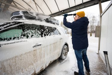 Man washing high pressure water american SUV car with roof rack at self service wash in cold weather.
