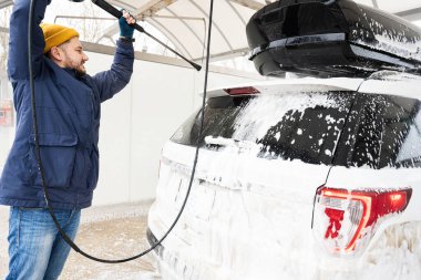 Man washing high pressure water american SUV car with roof rack at self service wash in cold weather.