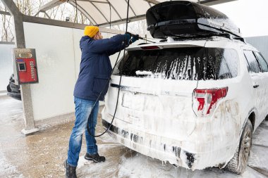 Man washing american SUV car with roof rack at a self service wash in cold weather.