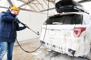 Man washing high pressure water american SUV car with roof rack at self service wash in cold weather.