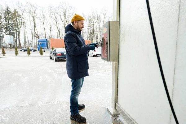 Man charges the device box with money at a self service wash in cold weather.