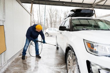 Man washing high pressure water american SUV car with roof rack at self service wash in cold weather.