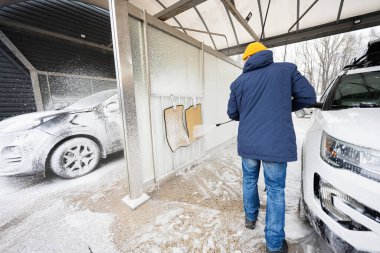 Man washing high pressure water american SUV car with roof rack at self service wash in cold weather.