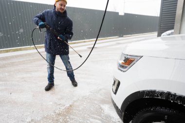 Man washing high pressure water american SUV car at self service wash in cold weather.