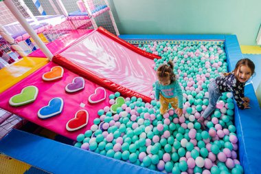 Kapalı oyun bahçesinde oynayan mutlu kız kardeşler, top havuzunda renkli toplar.