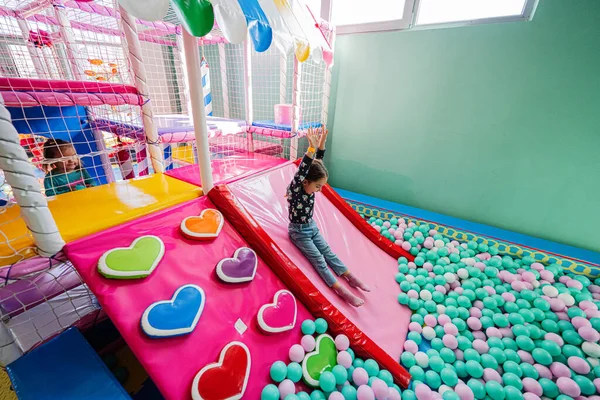 Happy girl playing at indoor play center playground. Sliding in color balls at ball pool.