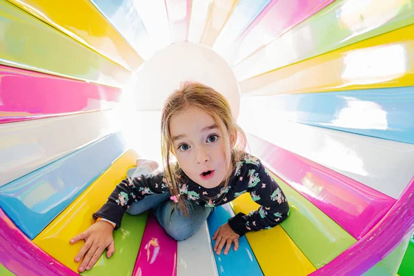 Funny girl playing at indoor play center playground in colored tube.