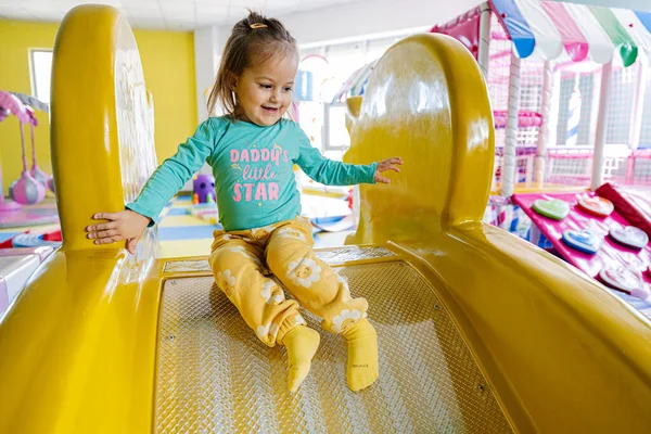 Happy girl playing at indoor play center playground. Sliding in yellow slide.