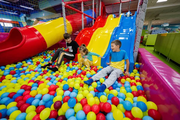 Happy kids playing at indoor play center playground. Children slides in colored slide into balls in ball pool.
