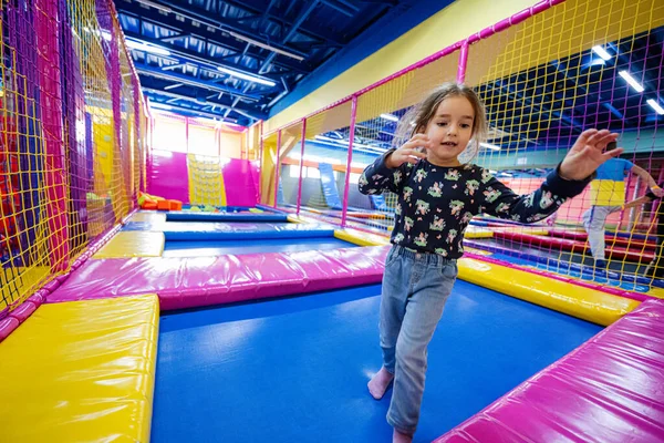 Happy kids playing at indoor play center playground. Girl jumping on trampoline.