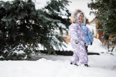 Children play outdoors in snow. Two little sisters near Christmas tree in winter. 