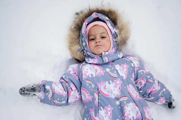 Baby girl making snow angel while lying on snow.