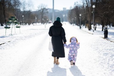 Back view of mother and child walking on a sunny frosty winter day in the park. Mom and daughter.