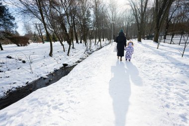 Back view of mother and child walking on a sunny frosty winter day in the park.