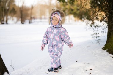 Baby girl wear child snowsuit on a sunny frosty winter day.