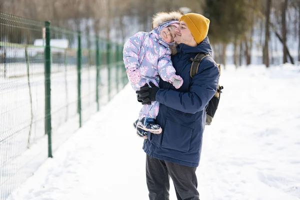 Father hold child on hands at sunny frosty winter day in the park. Dad and daughter love.