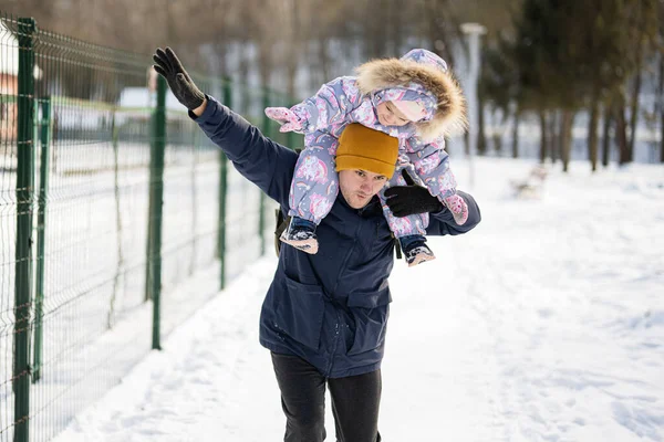 Father hold child on shoulders at sunny frosty winter day in the park. Dad and daughter love.