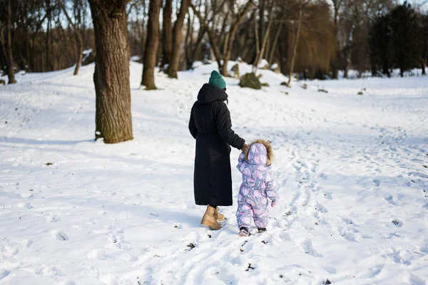 Back view of mother and child walking on a sunny frosty winter day in the park. Mom and daughter.