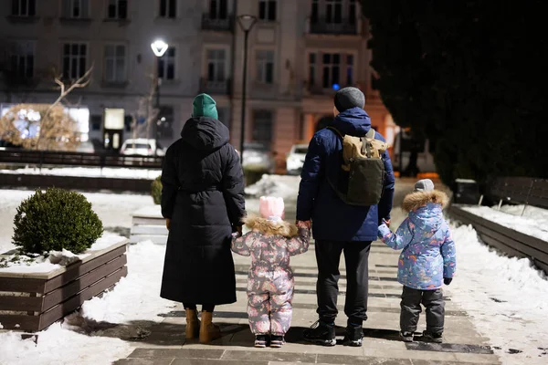 Back of family with two kids walk through the night city in the winter.