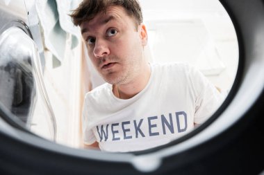 Man view from washing machine inside. Male does laundry daily routine.  Surprised facial expression.