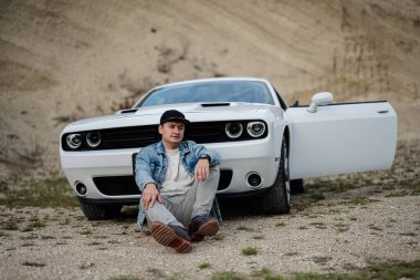 Kariyeri boyunca beyaz kaslı arabasının yanında oturan kot ceketli ve şapkalı yakışıklı bir adam..