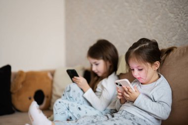 Two sisters wear pajamas playing phones early in morning.