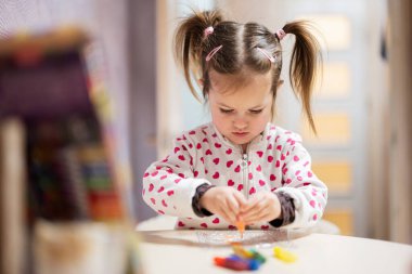 Baby girl with pigtails decorating art with glitter decor tube of paint.
